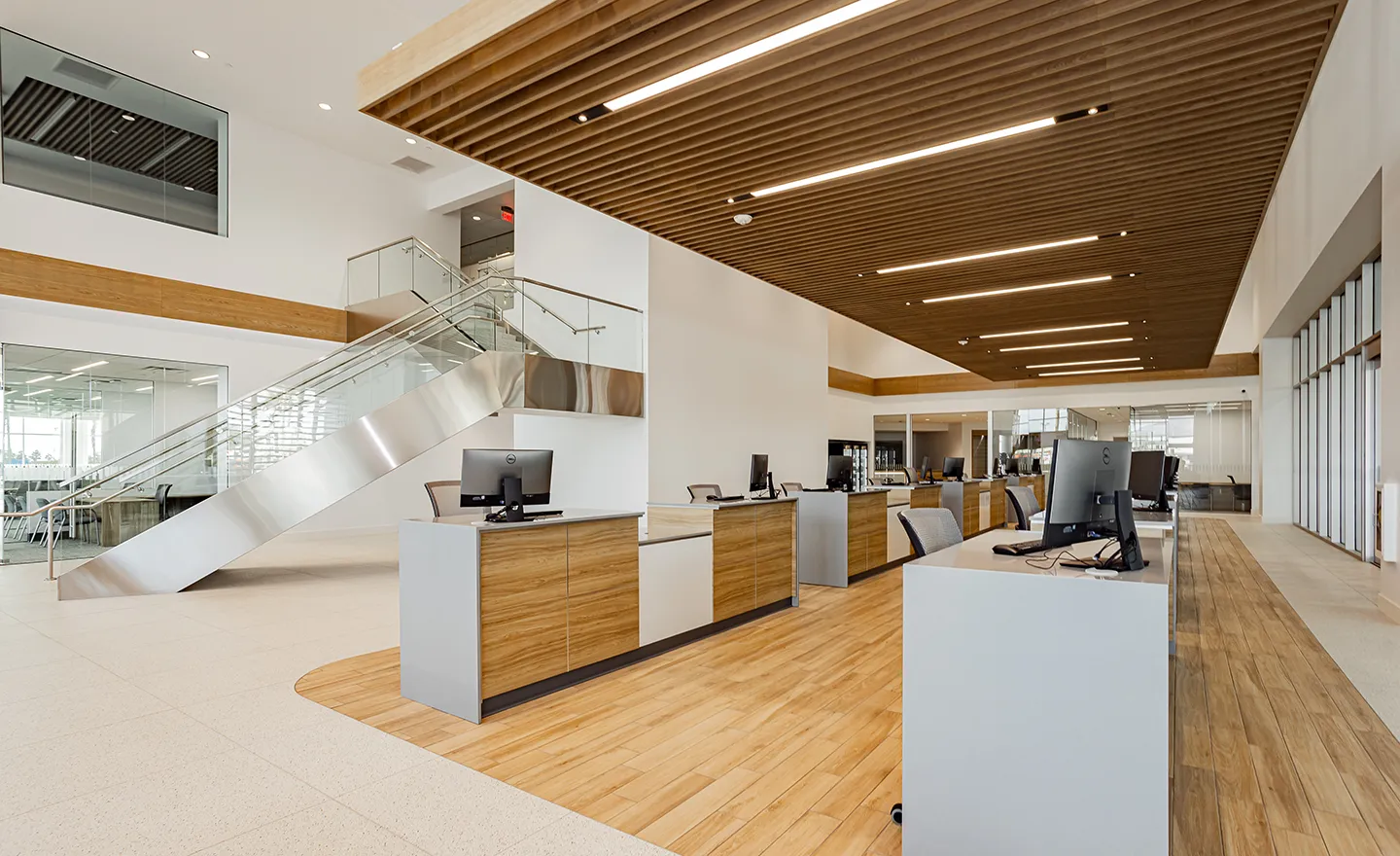 Modern office space with multiple workstations, a wooden floor, and a staircase leading to an upper level. The ceiling features wooden slats with recessed lighting installed by Adamik Electric, ensuring a well-lit and professional environment.
