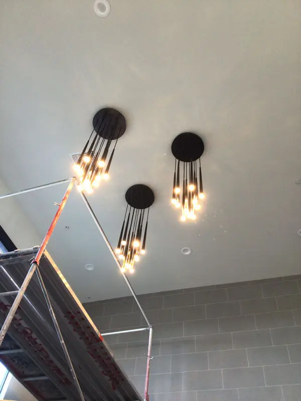 View of a ceiling with three modern pendant light fixtures emitting warm light, installed by Adamik Electric, and a metal scaffolding structure below in North Las Vegas.