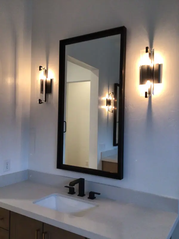 A bathroom vanity with a rectangular mirror, black frame, and two wall sconces on each side, above a white sink with black faucet fixtures installed by Adamik Electric in North Las Vegas.