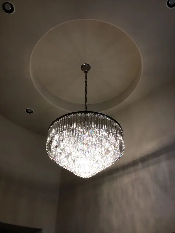 A chandelier with multiple crystal strands, installed by Adamik Electric, hangs from the ceiling in a circular recess, illuminated in dim lighting.