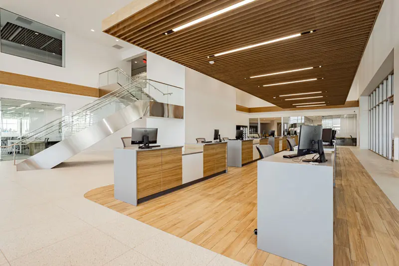 Modern office space with wooden accents, featuring several computer workstations on gray desks, a glass-walled meeting room to the left, and a metal staircase leading to an upper floor. This North Las Vegas gem is powered by reliable electric service courtesy of Adamik Electric.