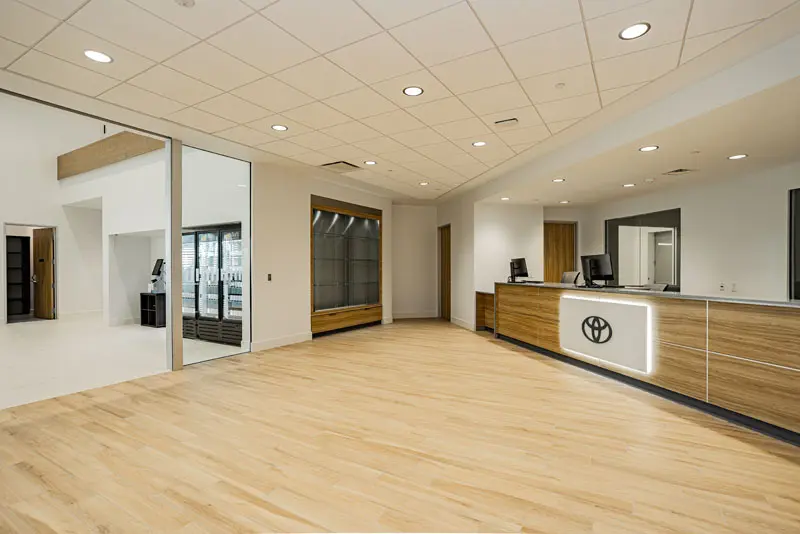 Spacious dealership showroom with wood flooring, a reception desk with a logo, modern lighting, and large windows in the background. Available in North Las Vegas, this location also offers convenient Tesla Charging for electric service vehicles.