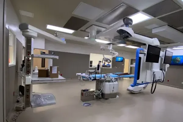 A modern medical operating room featuring advanced equipment and technology, including monitors, surgical tools, and overhead machinery, with neutral-toned walls and flooring.